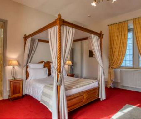 Le Domaine de Monrecour dispose de chambre avec un sol rouge et un lit en boiserie traditionnel entouré de draps faits en tissu noble